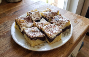 Babka zygzak z budyniem i śmietaną: Wilgotny deser z prostą dekoracją Babka zygzak z budyniem i śmietaną na blasze, udekorowana startą gorzką czekoladą